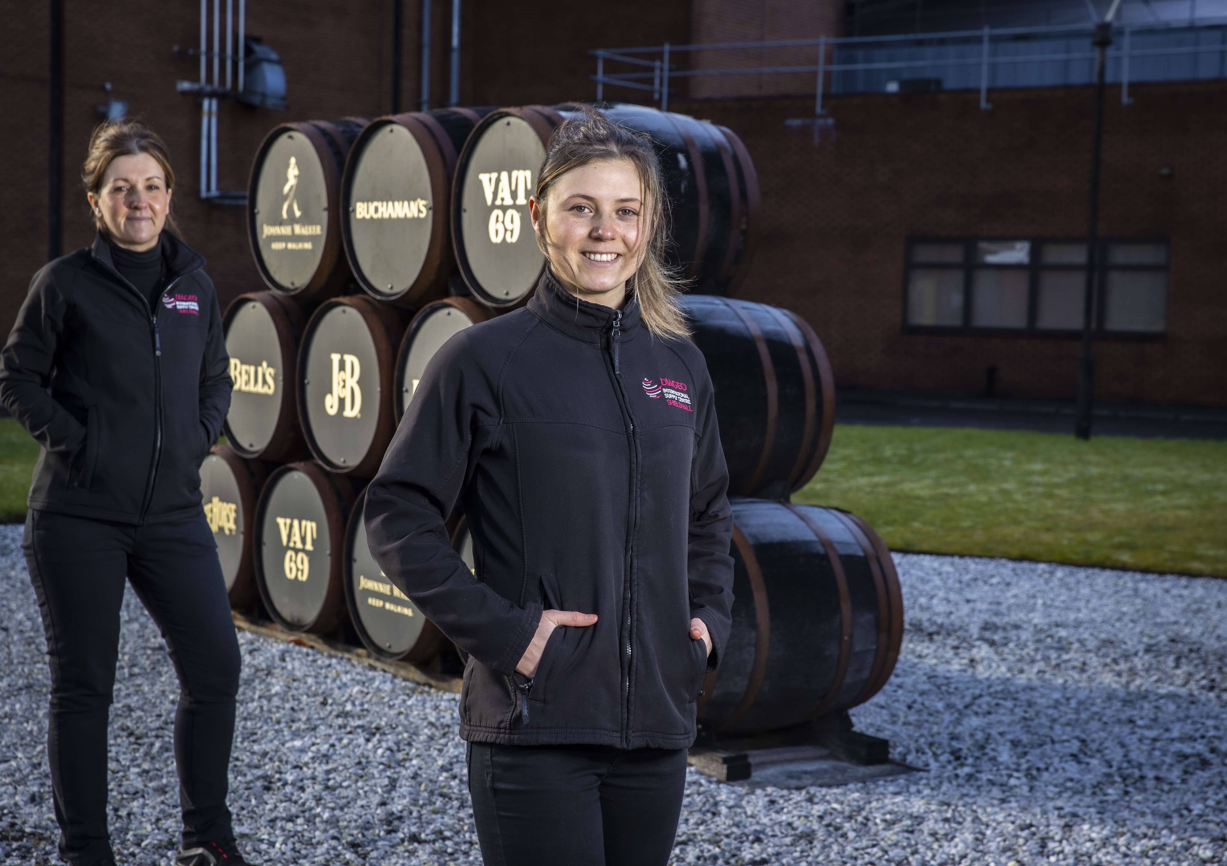 A woman standing in front of her supervisor with whisky barrels in the background.