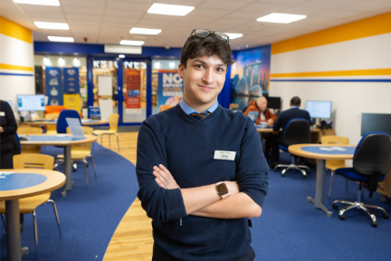 A young man stands with his arms folded in a travel agent shop.