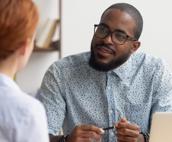 A man looking engaged as he chats to a woman across a desk.