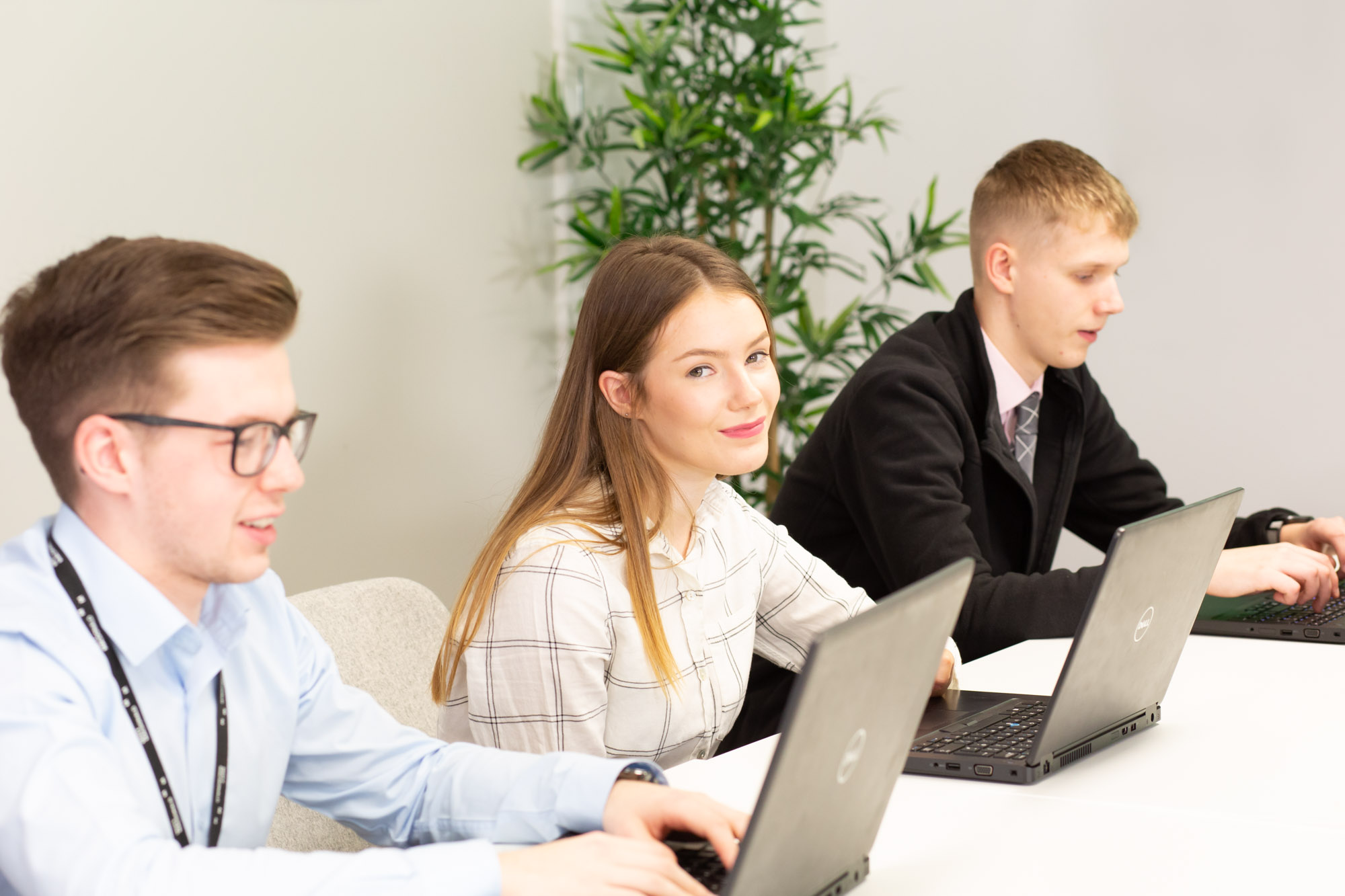 Three young people sitting down working on their laptops at a desk.