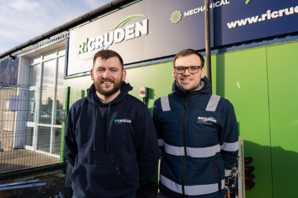 Two men, wearing blue work jackets, stand in front of RiCruden's premises.