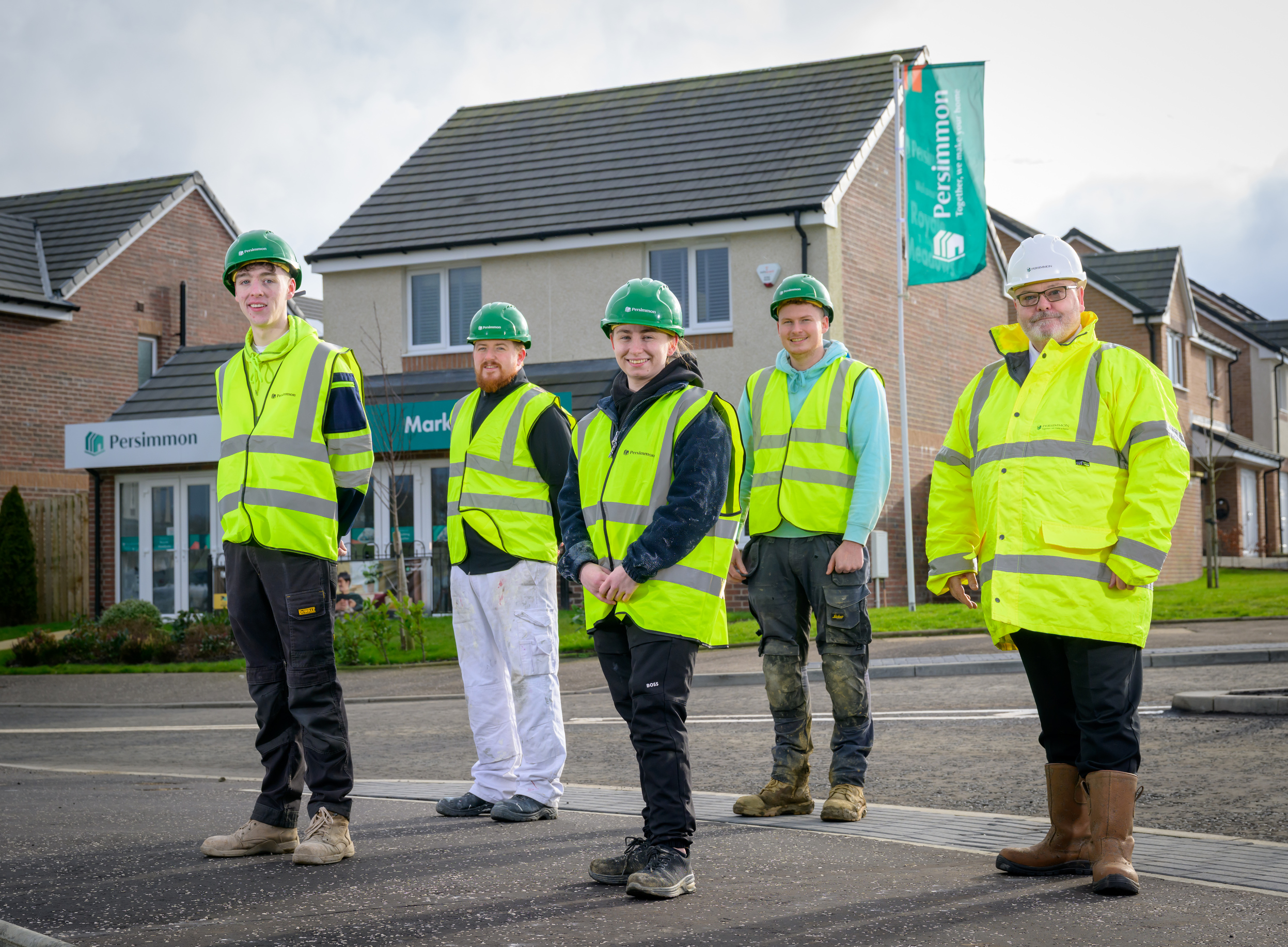 A group of people, all wearing hi-vis vests, stand in front of a new-build housing estate.