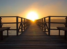 A boardwalk at the seaside with the sun in the horizon.