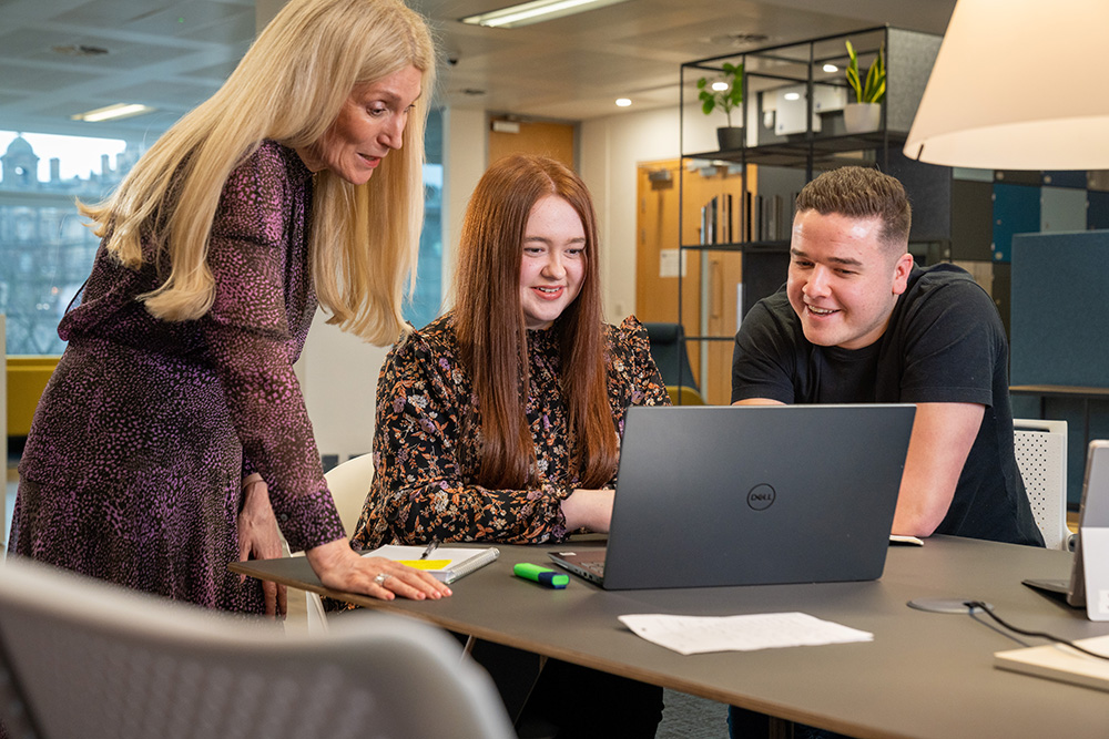 An older colleague giving advice to two younger members of staff as they all look at a laptop screen.