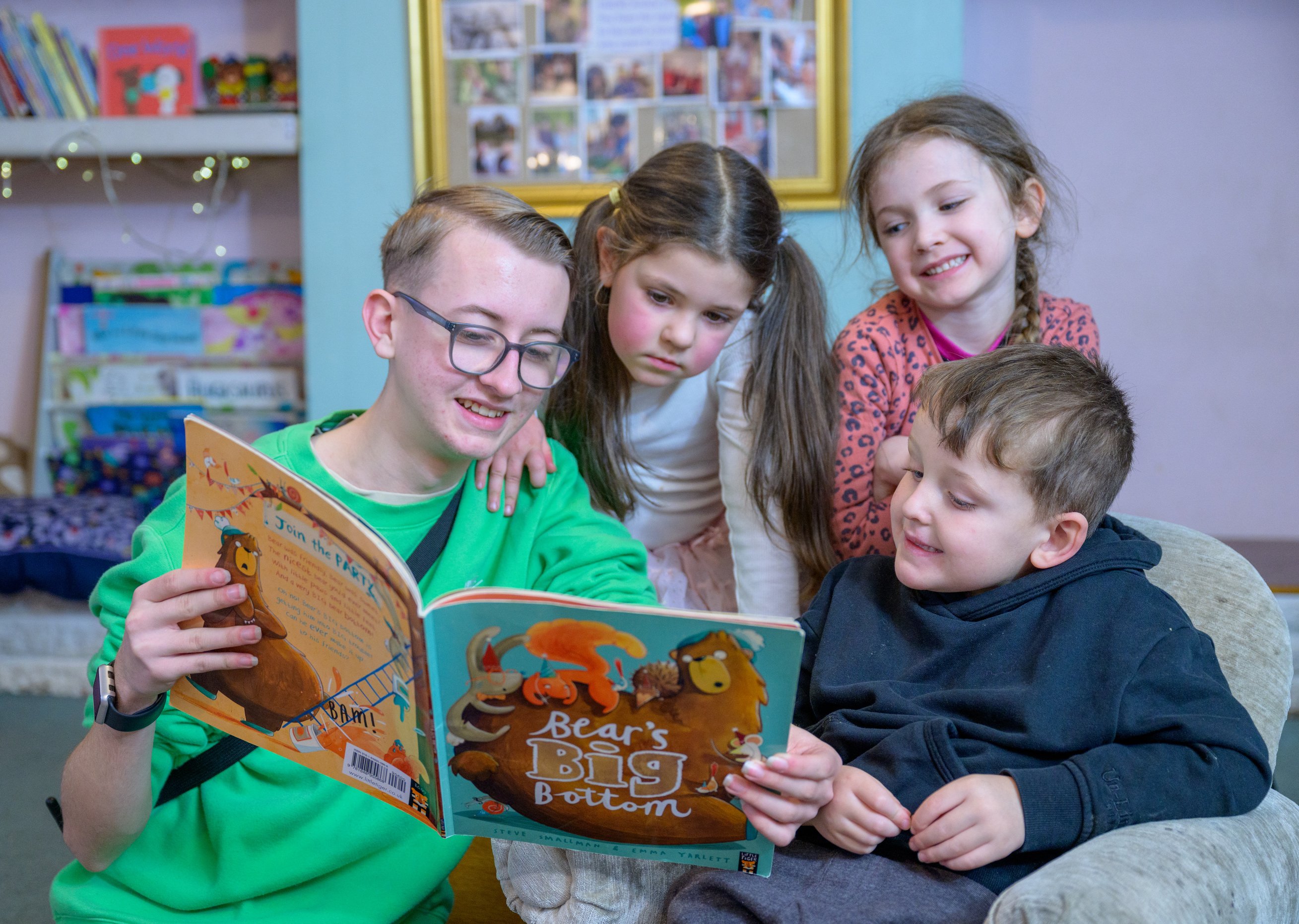 A person reads a book to three nursery children.