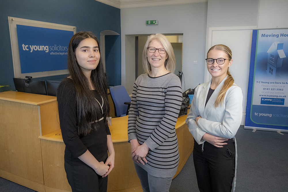 Three women smiling with a reception desk behind them.