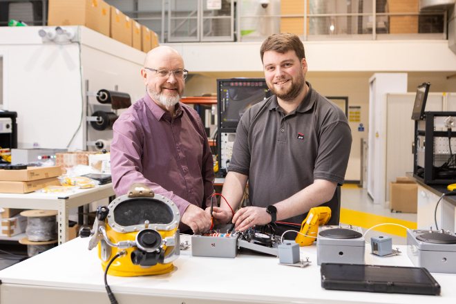 Two men stand at a work bench.