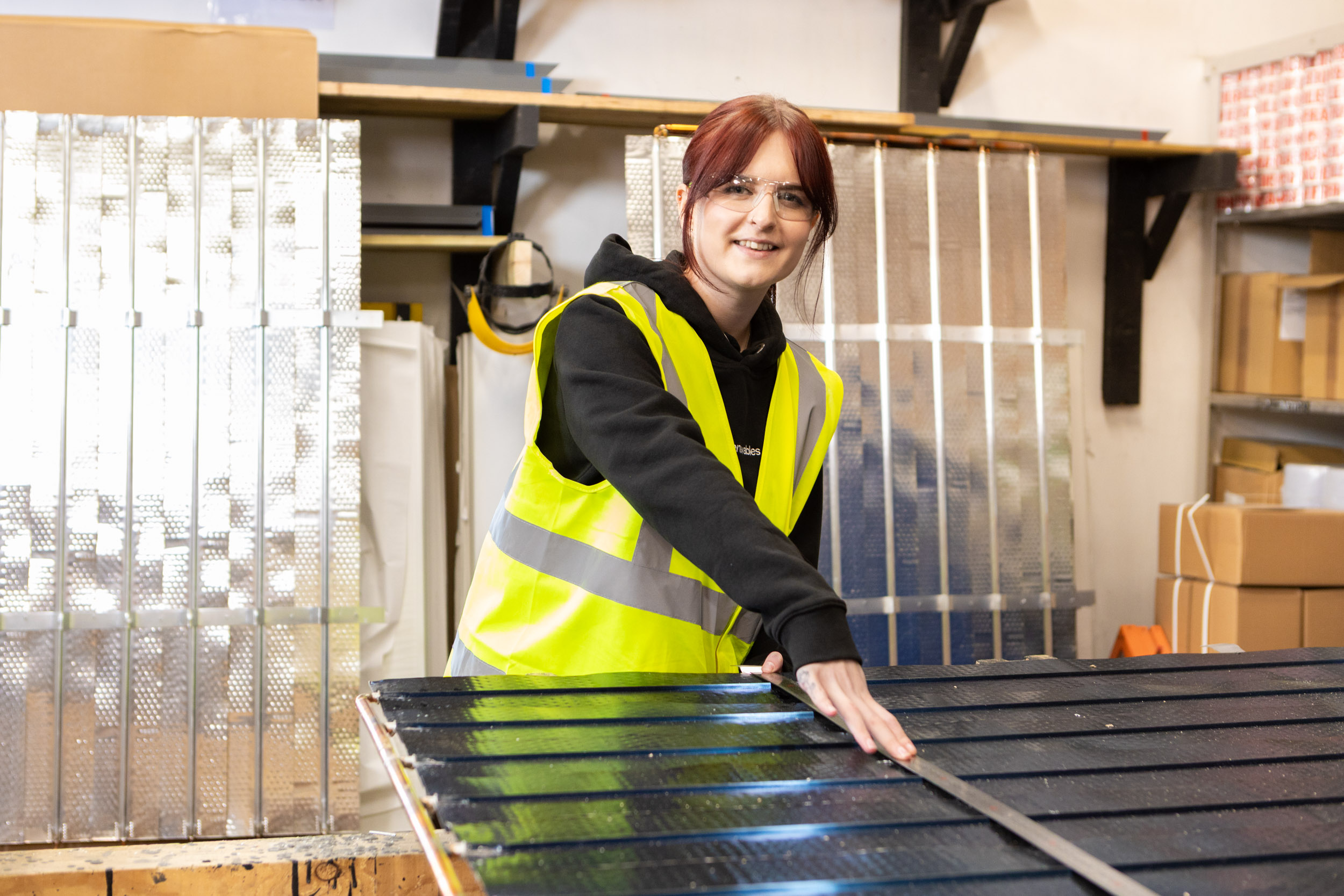 A young woman, wearing a hi-vis vest, measures a sheet of metal.